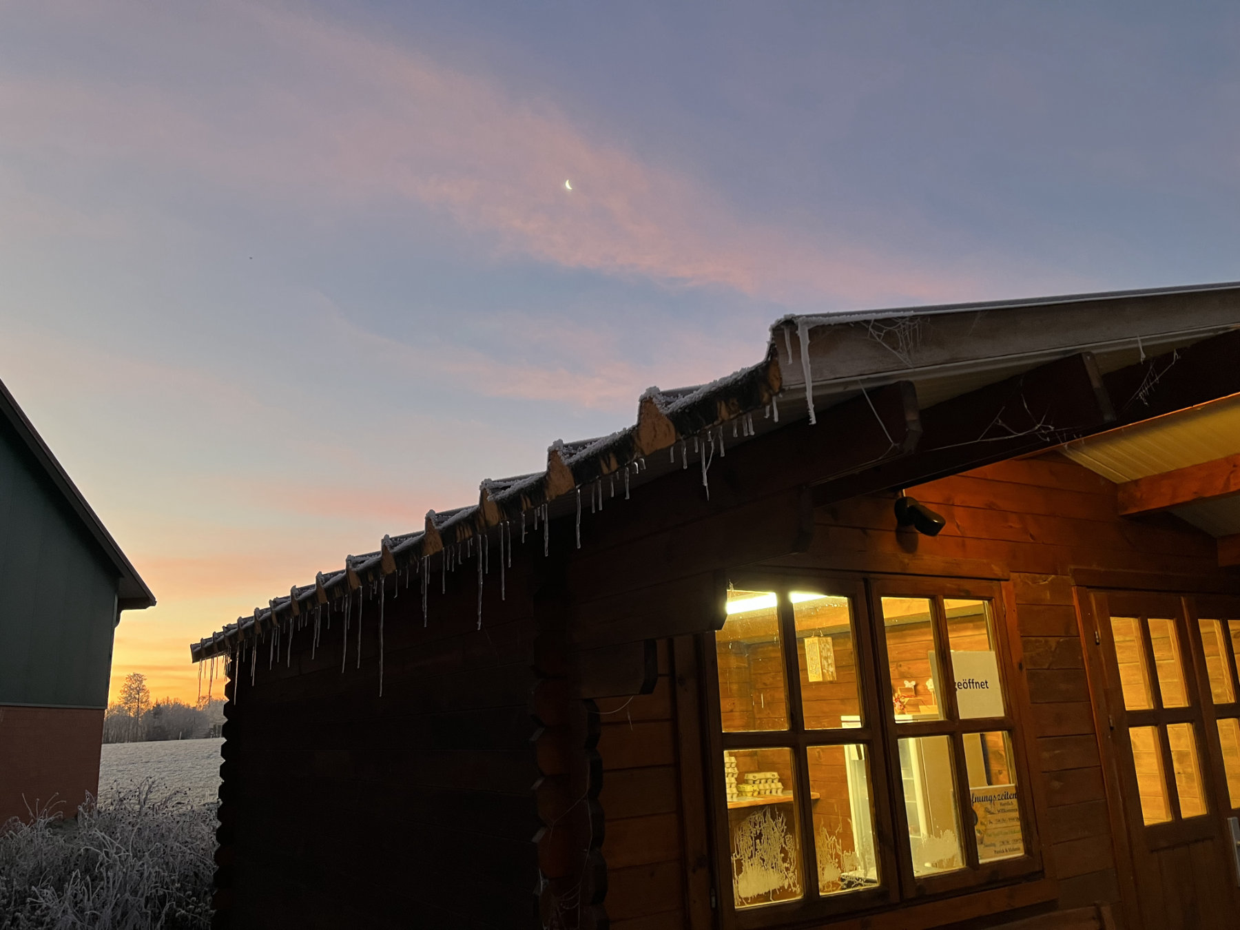 Beleuchtete Holzhütte im Winter mit Eiszapfen